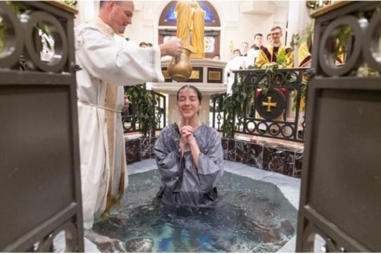 En ung kvinna döps vid påskvakan 2024 på St. Mary's Catholic Center i Texas A&M.