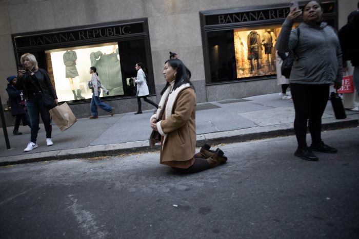 En kvinna knäböjer när den eukaristiska processionen som sponsras av Napa Institute passerar förbi på gatorna i New York City den 15 oktober 2024.